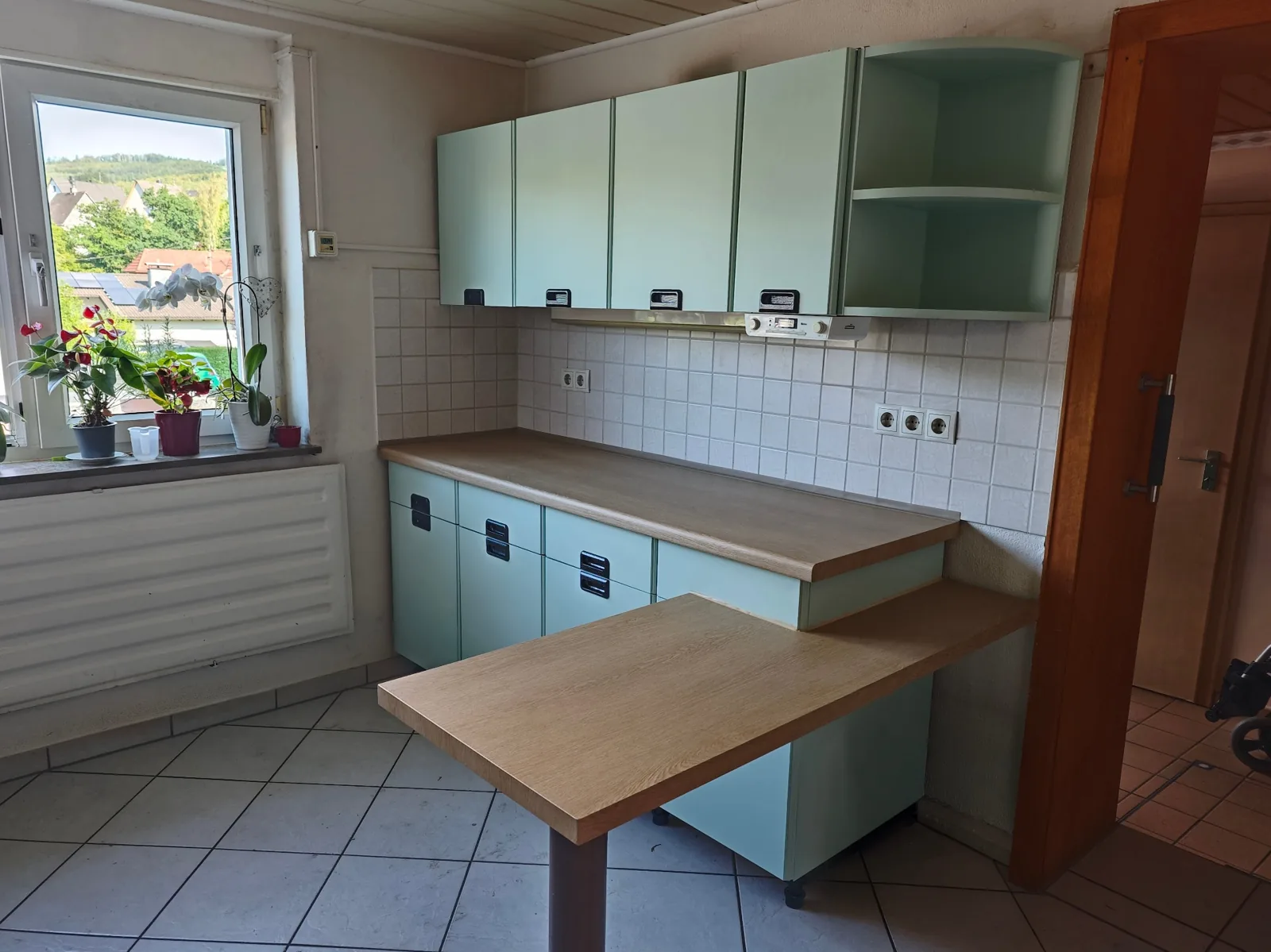 Heller Essbereich der folierten Küche in Mintgrün mit Blick zum Fenster und neuer Arbeitsplatte in Eichenoptik