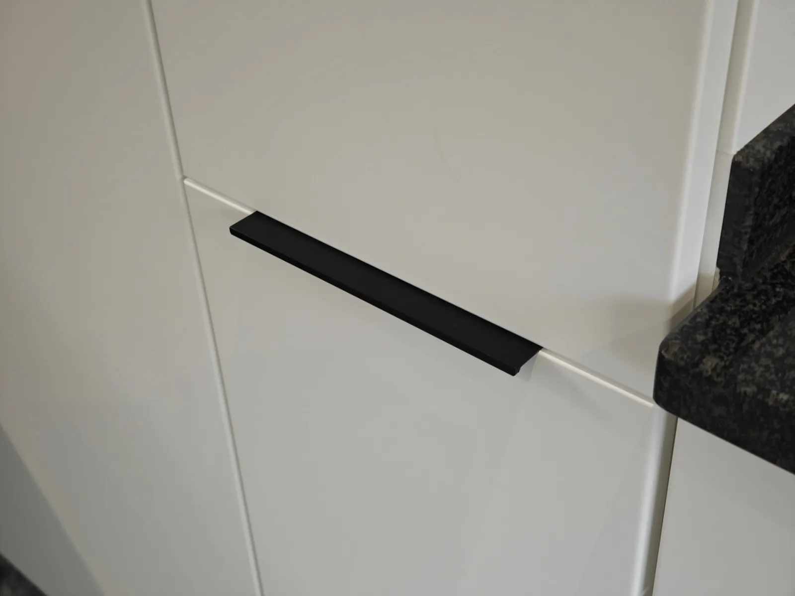 Detailaufnahme eines schlanken schwarzen Profilgriffs auf einer matt-weiß folierten Küchenfront