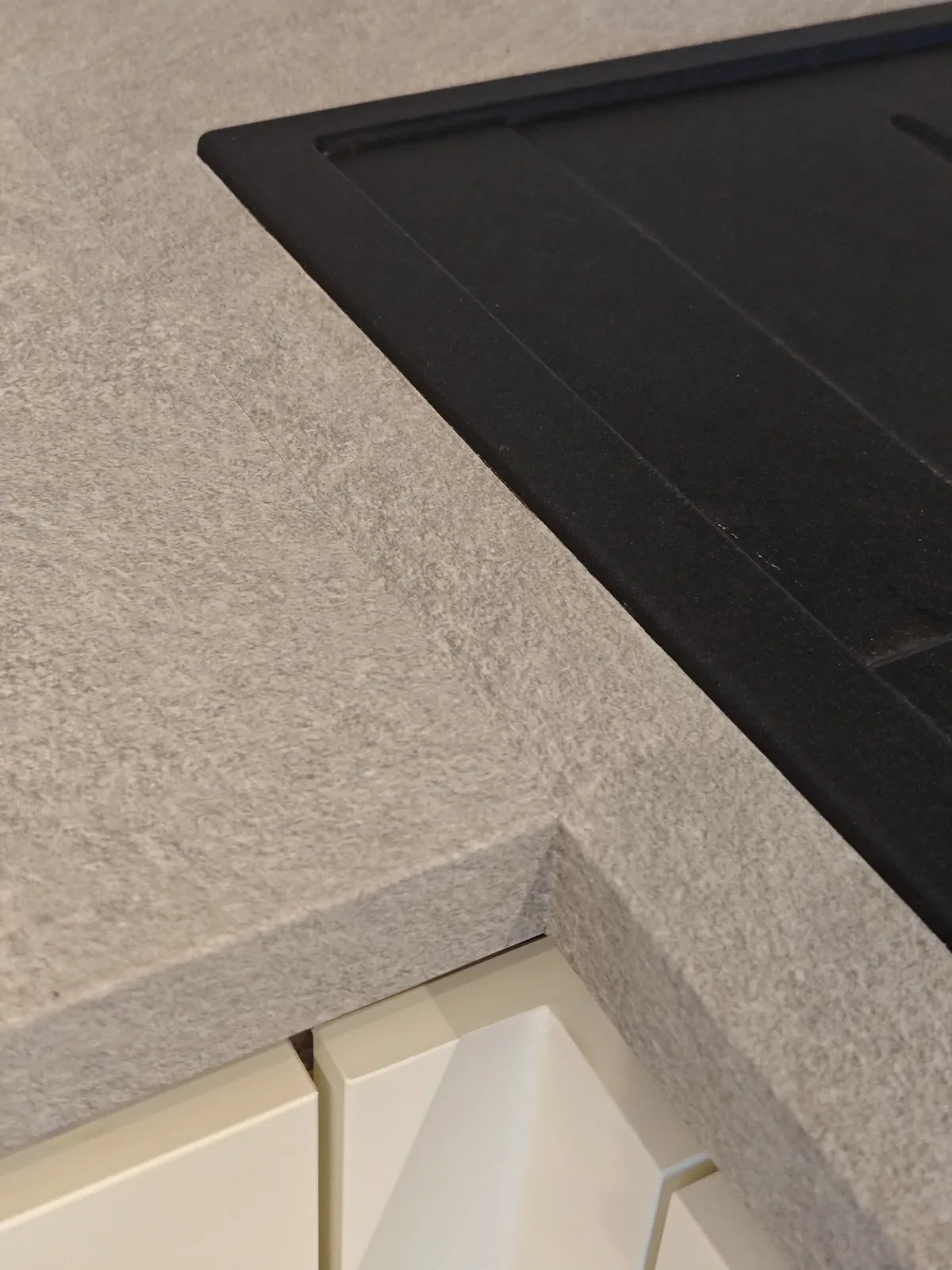 Nahaufnahme der folierten Arbeitsplatte in Betonoptik: fühlbare Struktur, sauber gearbeitete Ecke und Kante am Ausschnitt der schwarzen Spüle