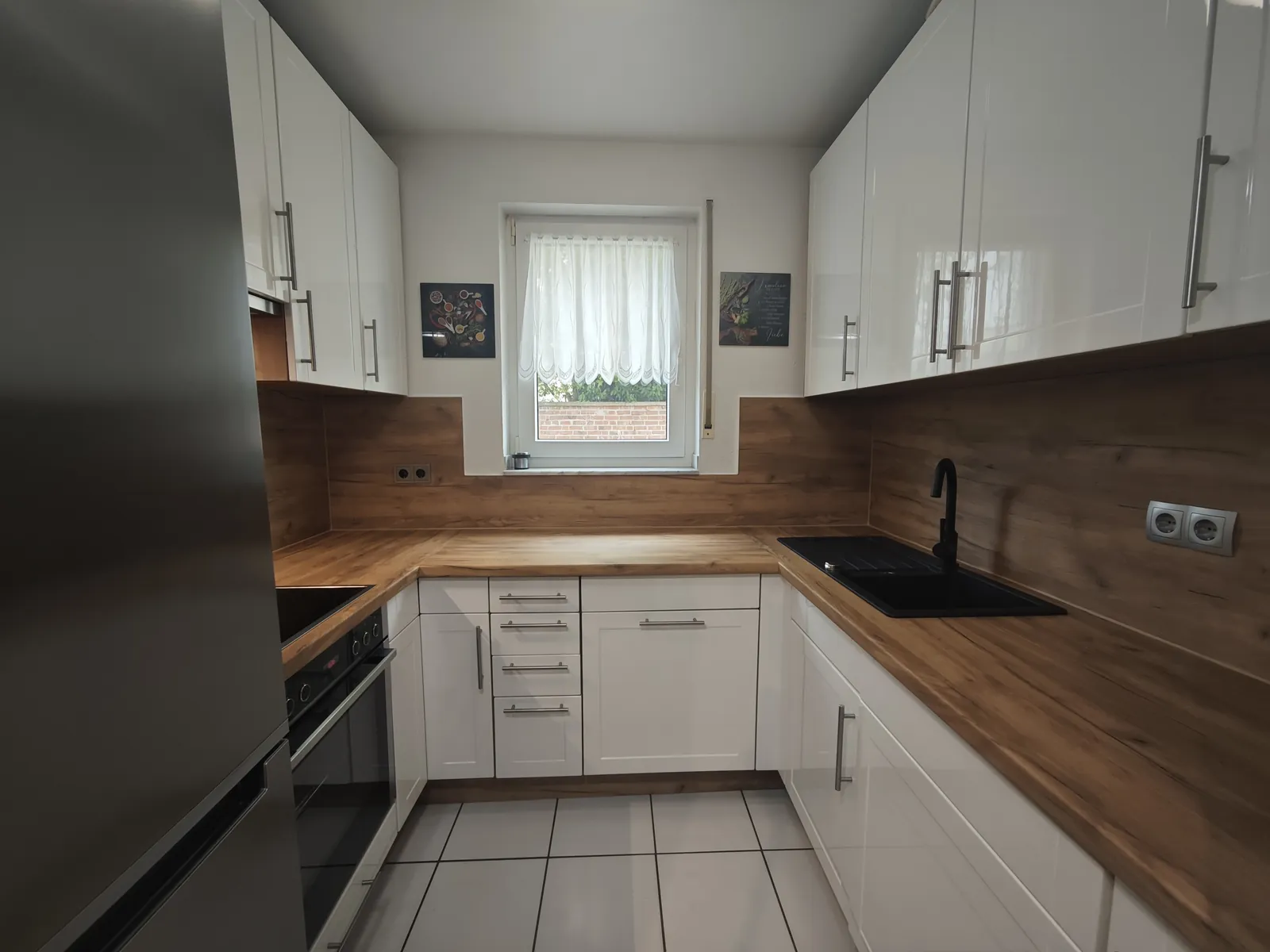 Kleine U-Küche mit weißen Hochglanzfronten, Arbeitsplatte und Küchenrückwand in Eichenholz-Optik foliert, schwarze Spüle mit schwarzer Armatur