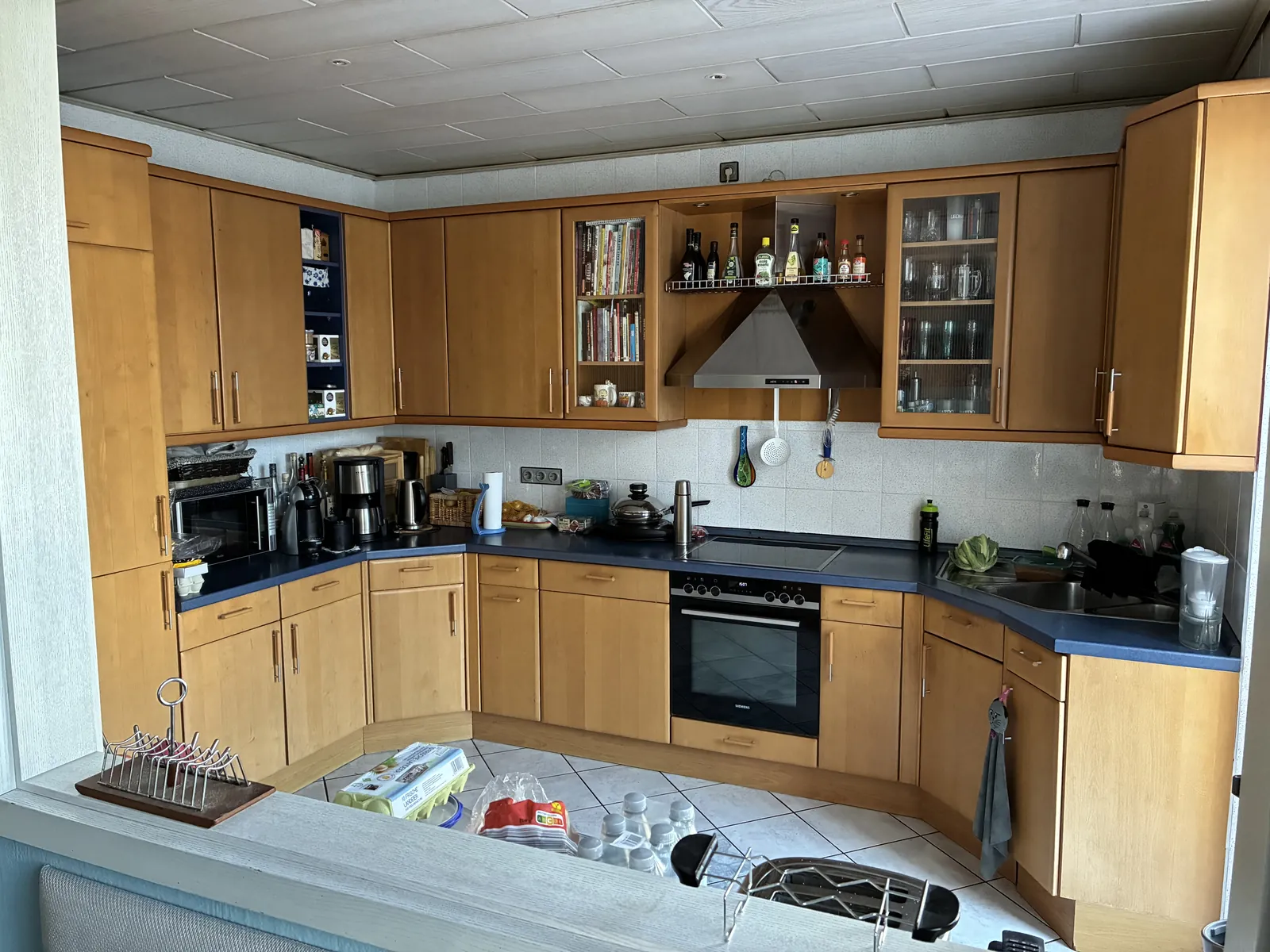 Küche vor der Renovierung: Fronten in Buche, weißer Fliesenspiegel mit kleinen Fliesen, dunkelblaue Arbeitsplatte, Edelstahl-Dunstabzug